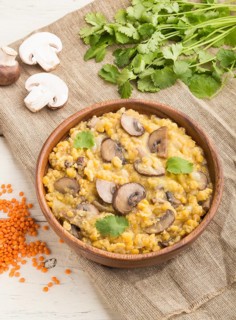 Lentils porridge with champignons and coriander in a wooden bowl on a white wooden background and