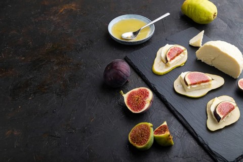 Summer appetizer with pear, cottage cheese, figs and honey on slate board on a black concrete