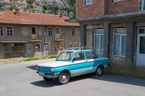 A blue retro car parked in front of dilapidated buildings under a clear sky, Zaporozhets 968,