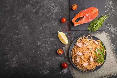 Semolina pasta with salmon and salmon steak on a black concrete background and linen textile. Top