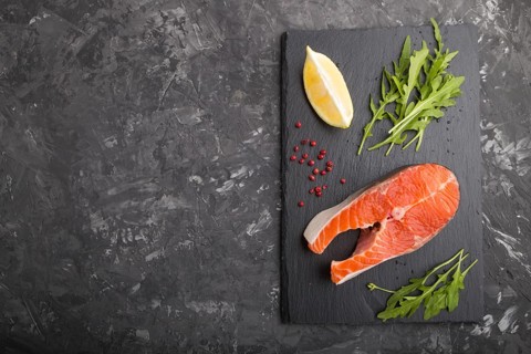Raw salmon steak with arugula and lemon on a black slate board on a black concrete background. Top