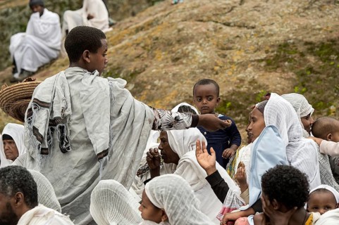 Altar boy distributes blessed bread to worshippers in traditional white Shamma dress after the