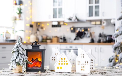 Cozy Christmas decor tiny house of small size on table of festive white modern kitchen. Gift for