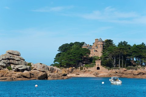 Historic castle on a rocky island surrounded by clear blue sea with a small white boat, granite