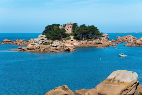Picturesque island with historic building and rocks, surrounded by deep blue water and sunny skies,