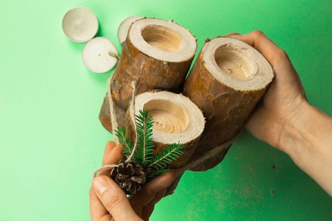 DIY Christmas candle holder made of pine logs, candles, craft rope, fir branches and cones. Hands
