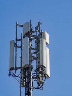 A close-up of a cell tower with antennas against a bright blue sky