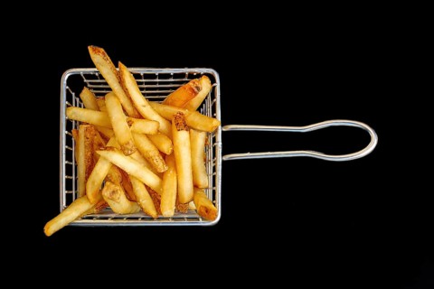An aerial perspective of a modest basket containing French fries, set against a dark backdrop