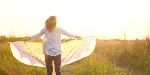 Girl is standing with wings in field, learning to fly a kite, Outdoor entertainment in summer,