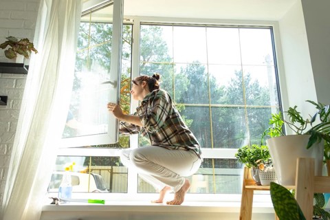 Woman manually washes the window of the house with a rag with spray cleaner and mop inside the