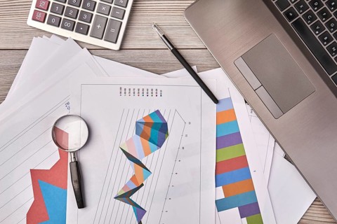 Papers with charts and glass magnifier with pen. Laptop device with calculator top view
