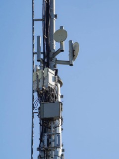 Telecommunication tower against a clear blue sky, featuring antennas, microwave dishes, and