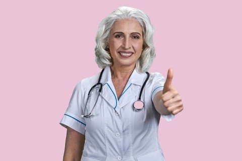 Successful senior woman doctor gesturing thumb up to camera. Joyful female doctor giving thumb up