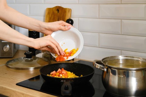 Closeup view of female hand puts chopped vegetables in a frying pan. Process of preparation of