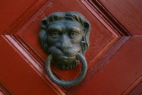 Traditional metal lion's head door knocker on a red wooden door, detail, Klingenstein Castle,