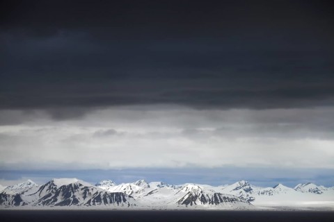 Black rain clouds over snow covered mountains along Isfjorden, second longest fjord at Spitsbergen,