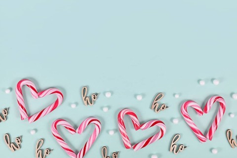 Small red and white striped Christmas candy cane sweets forming heart on blue background with copy
