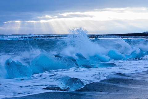 Waves breaking on icebergs on the black beach of Breidamerkursandur, near Jökullsarlon, Sudurland,