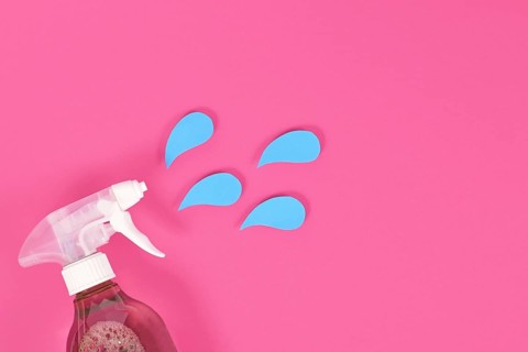 Cleaning agent spray bottle with blue liquid drops cut from paper on pink background