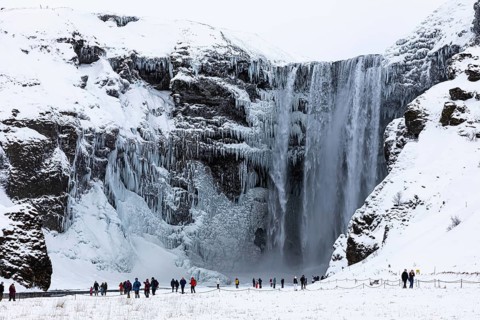 Tourists at Skogafoss waterfall, snowy and icy rock face, Sudurland, Iceland, Europe
