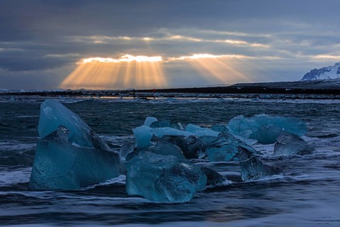 Waves breaking on icebergs on the black beach of Breidamerkursandur, sunset, near Jökullsarlon,