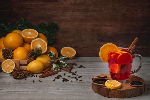 Wooden basket with oranges and lemons, punch in glass cup, cloves and cinnamon sticks, Christmassy,
