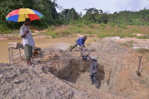 Diamond hunters digging a pit with shovels, supervisor holding a parasol, left, near Koidu,