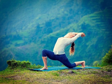 Yoga outdoors, sporty fit woman practices Hatha yoga asana Anjaneyasana, low crescent lunge pose