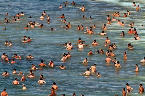 View from above of anonymous crowd on the beach, tourists swimming in the sea, enjoying cooling