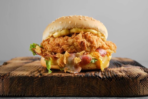 Chicken burger with bacon and cheese on wooden board, front view