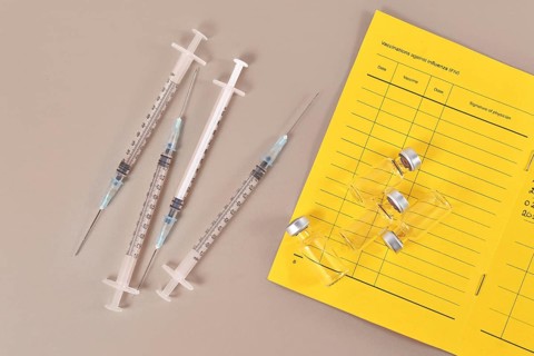 Concept for Corona virus booster vaccination showing vaccine passport with 4 syringes and vials