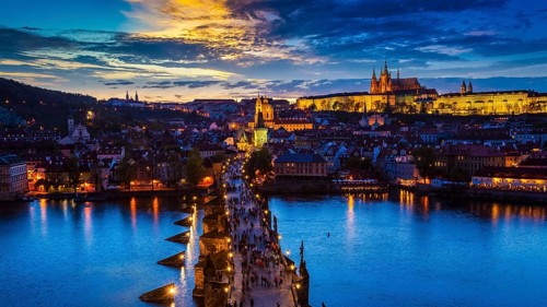 Panorama of illuminated Prague castle and Charles Bridge with tourist crowd over Vltava river in