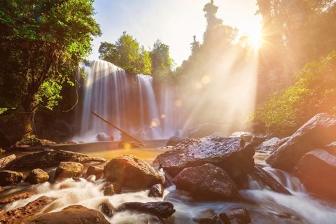 Tropical waterfall in the morning with sun rays in Cambodia. Lens flare and light leak
