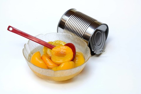 Peach, pickled peach halves in glass bowl with ladle and preserving tin