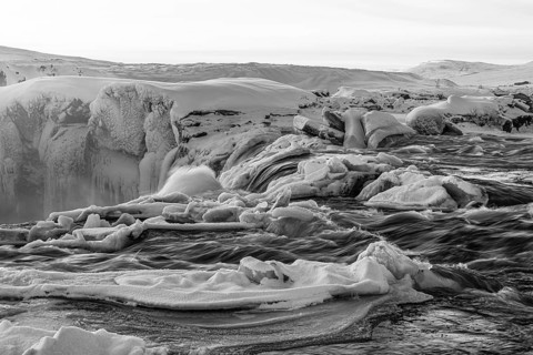 Icefall at the edge of the Godafoss waterfall at dawn, snow-covered landscape, black and white