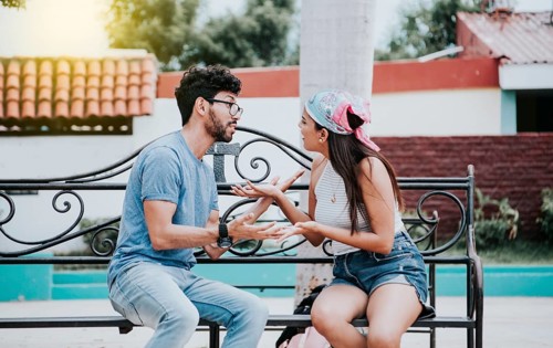 Man arguing with his girlfriend sitting in a park. Young couple arguing sitting on a park bench,