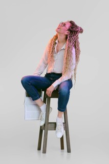 Woman with dreadlocks sits on tall chair, holds magazine in hand and looks up