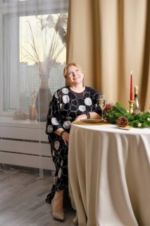 Joyful middle age woman celebrating christmas sitting behind the festive table