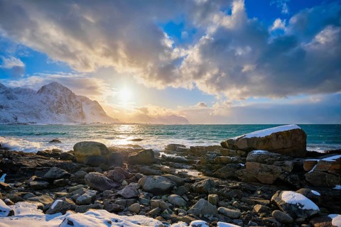 Beach of Norwegian sea on rocky coast in fjord on sunset in winter. Vareid beach, Lofoten islands,