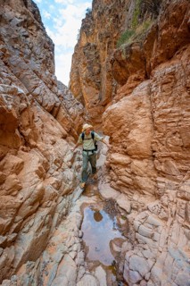 Mountaineers in a narrow canyon with a dry stream bed, eroded mountain landscape with red sandstone