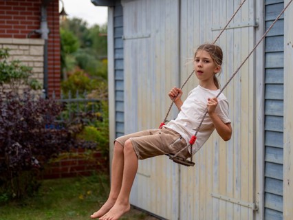 Boy swinging while sitting on children's swing at shed and garden gate, Germany, Europe
