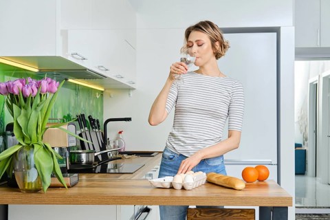 Beautiful young woman drinks water before making breakfast in her kitchen
