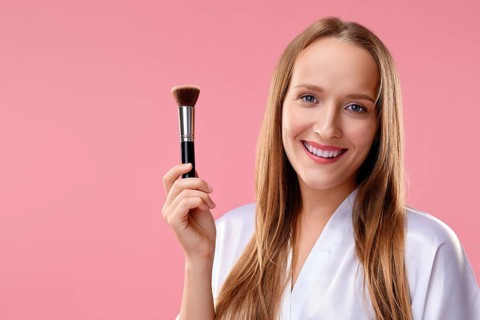 Beautiful girl with makeup brush in hand over pink background