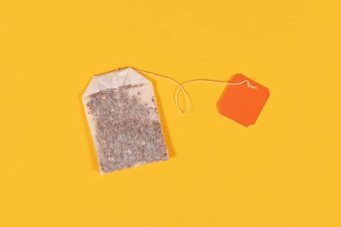 Tea bag with blank orange label on yellow background