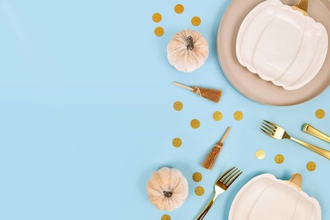 Halloween party flat lay with cream colored pumpkin shaped plates, witch brooms and golden confetti