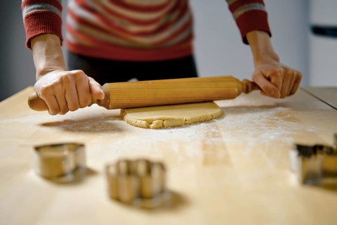Unrecognizable woman rolls out ginger dough with rolling pin on kitchen table (low angle view with