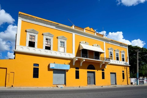 Two-storey yellow building under a clear blue sky with closed shop fronts, Church of Christ,