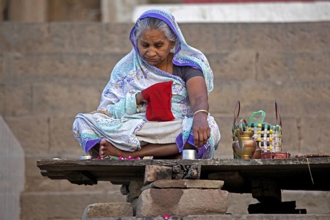Old Indian woman sitting on ghat and praying near the Ganges river at Varanasi, Uttar Pradesh,