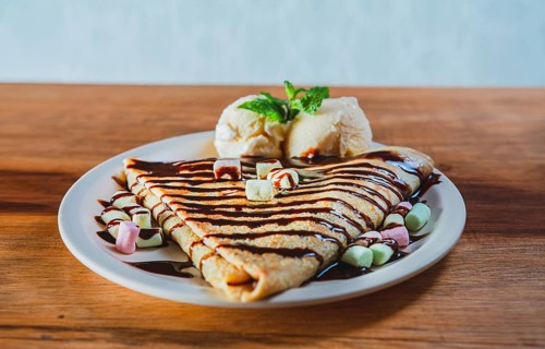 Close up of sweet crepe with ice cream on wooden table. Chocolate crepe with ice cream on wooden