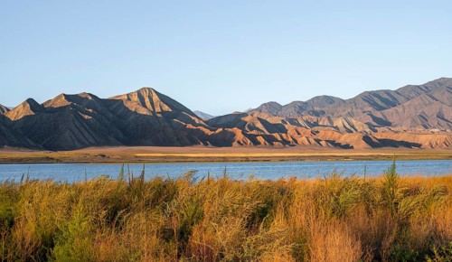 Blue Toktogul reservoir between dry mountain landscape, hilly mountains in the evening light,